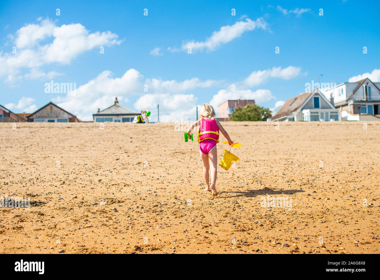 A cute, pretty little girl carrying a yellow bucket walking on the
