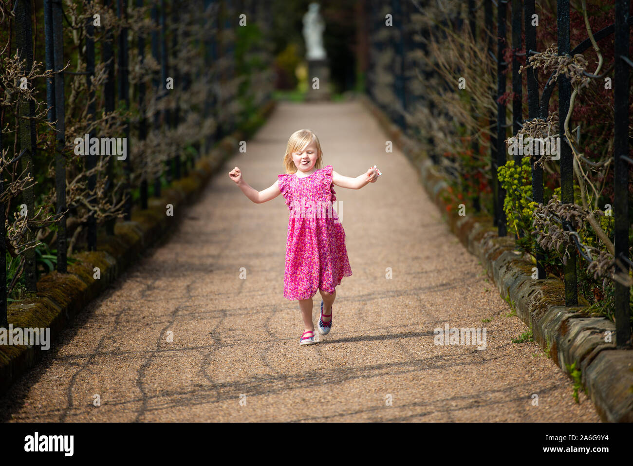 A cute, pretty little girl in a pretty pink dress skipping through a ...
