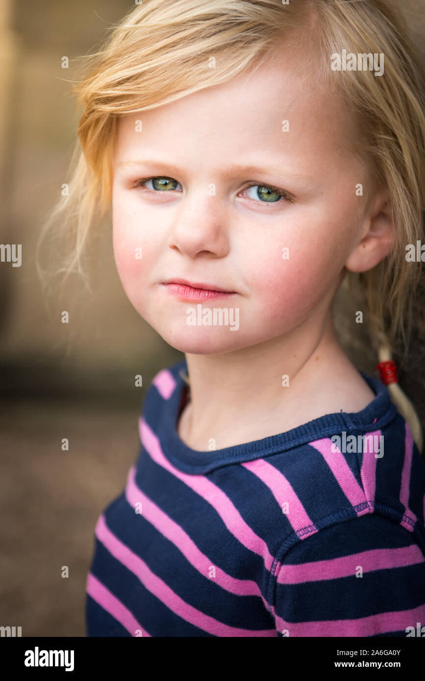 A pretty little girl with blonde hair and bright green eyes standing  against a wall at Trentham Gardens on a family day out in the country Stock  Photo - Alamy