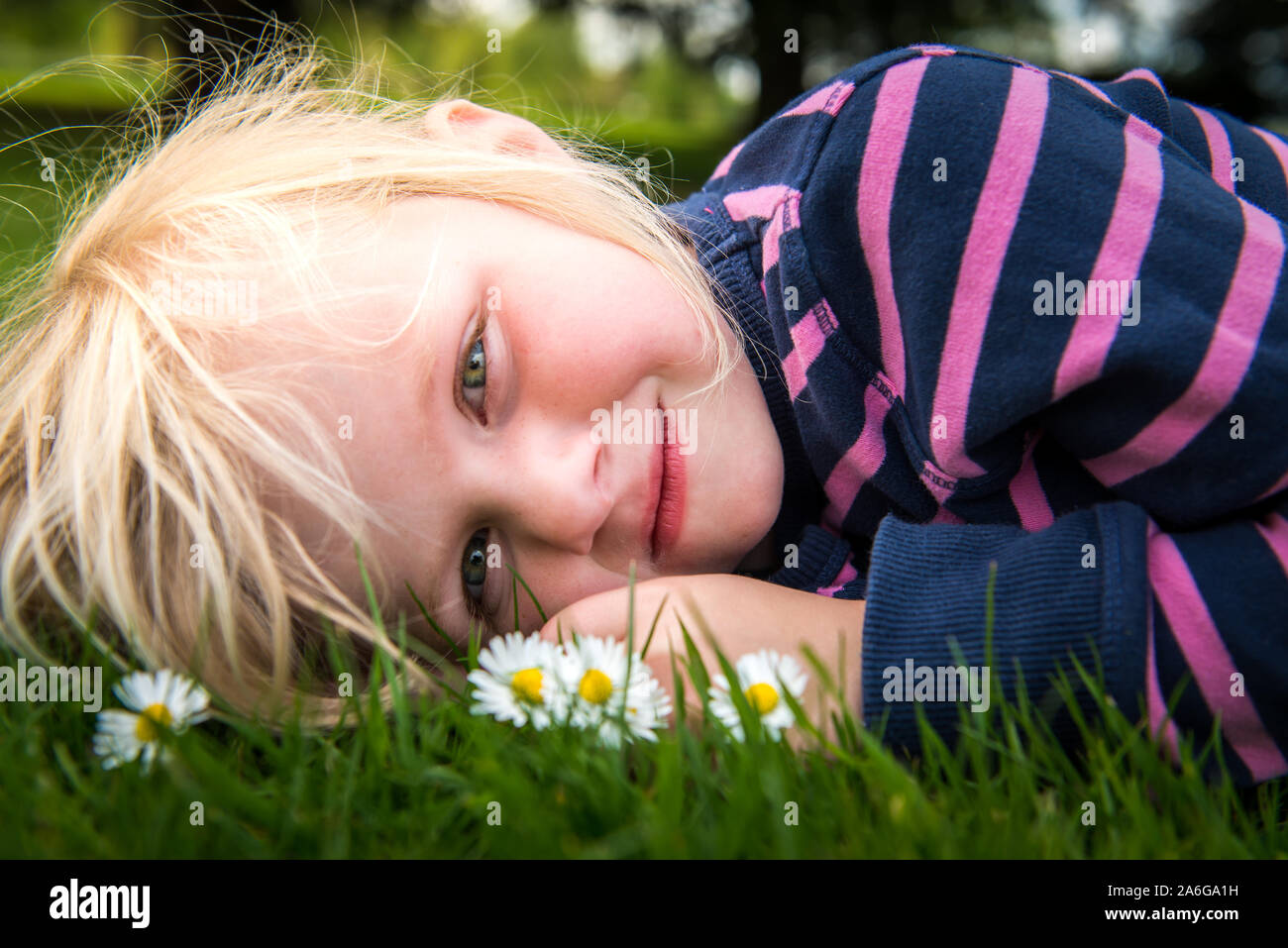 A pretty little girl with blonde hair and bright green eyes lying on ...