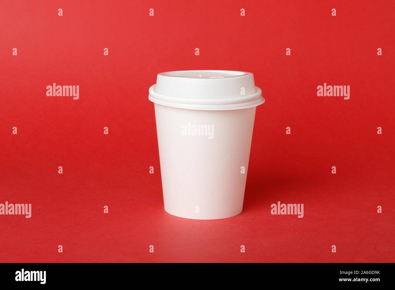 One white disposable paper cup with attached plastic lid on red background. Stock Photo