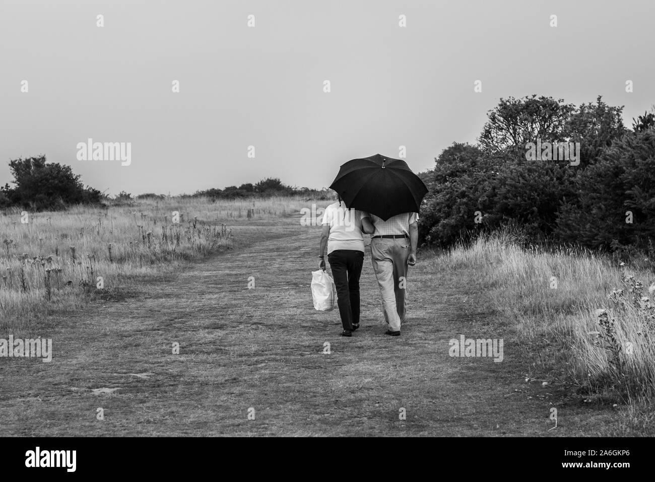 An elderly couple walking under an umbrella in Walton on the Naze, Essex Stock Photo