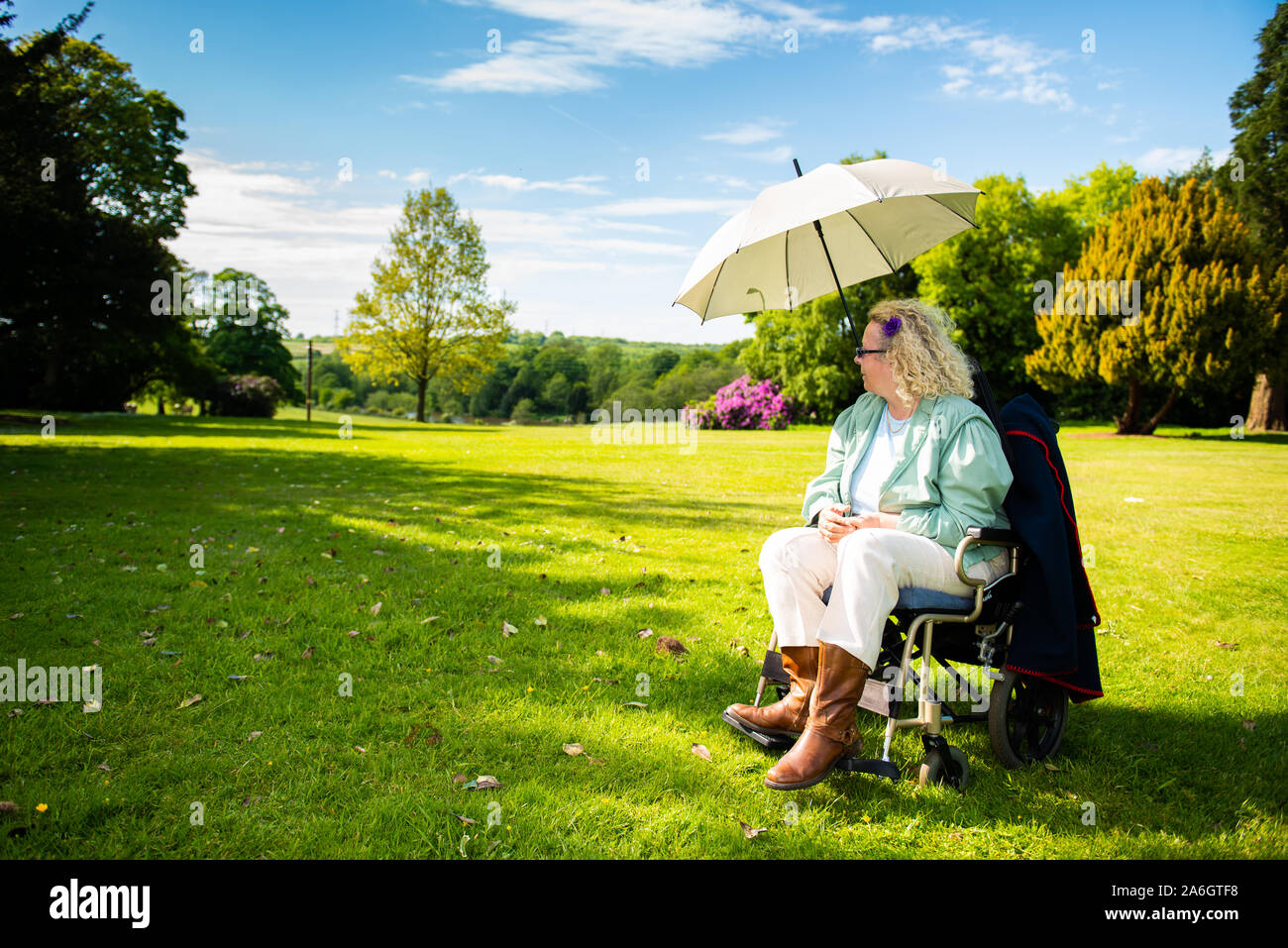 A disabled lady sits in her wheelchair on a hot summers day under an umbrella to keep her cool and in the shade, Stroke, heart attack, illness Stock Photo