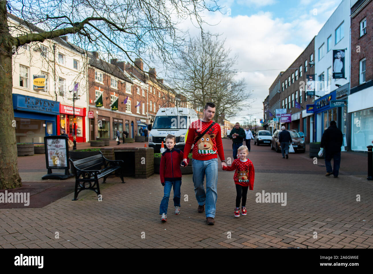 A father walks holding the hands of his two children wearing Christmas jumpers on Xmas eve Stock Photo