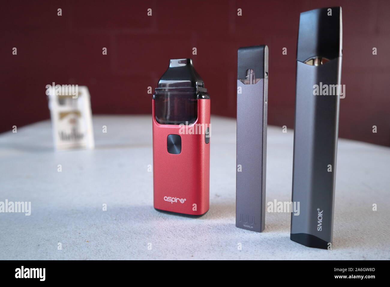 3 different vape pen electronic cigarette devices juul, aspire breeze, smok infinix, with a pack of Marlboro Gold cigarettes in the background out of Stock Photo