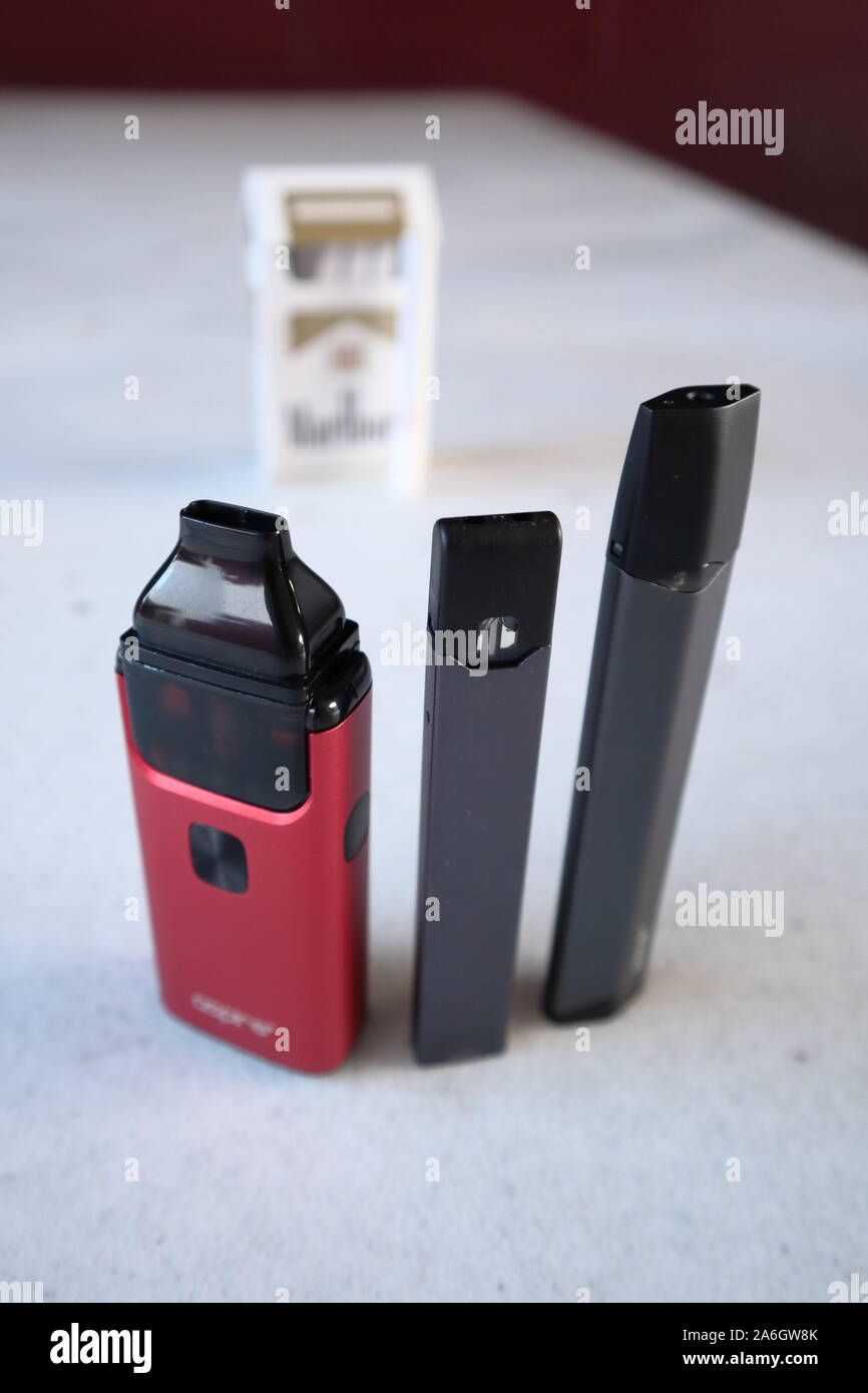 3 different vape pen electronic cigarette devices juul, aspire breeze, smok infinix, with a pack of Marlboro Gold cigarettes in the background out of Stock Photo