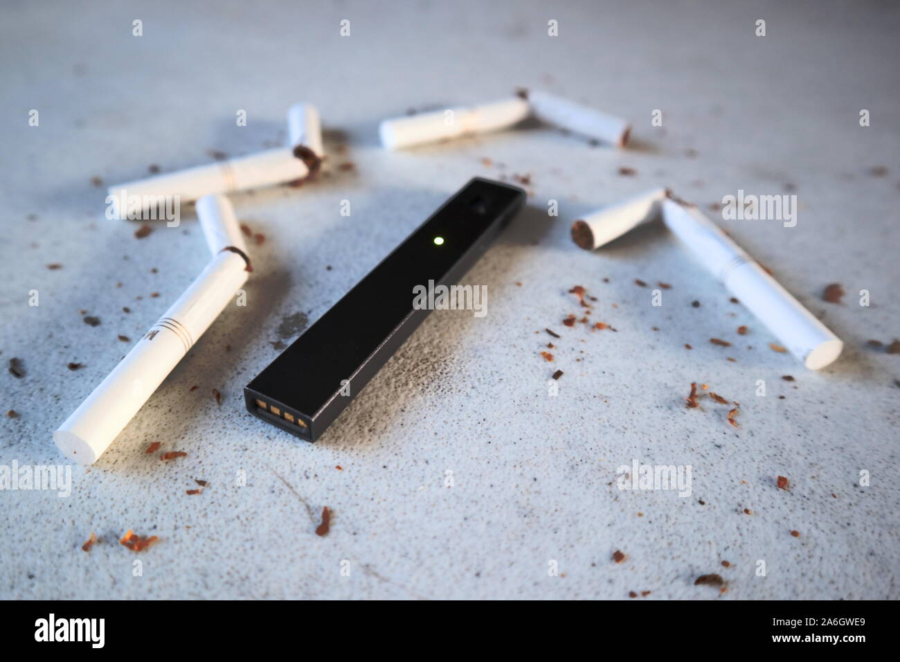 Vape device electronic cigarette juul, as smoking alternative with broken marlboro gold cigarettes and scattered tobacco on white textured background Stock Photo