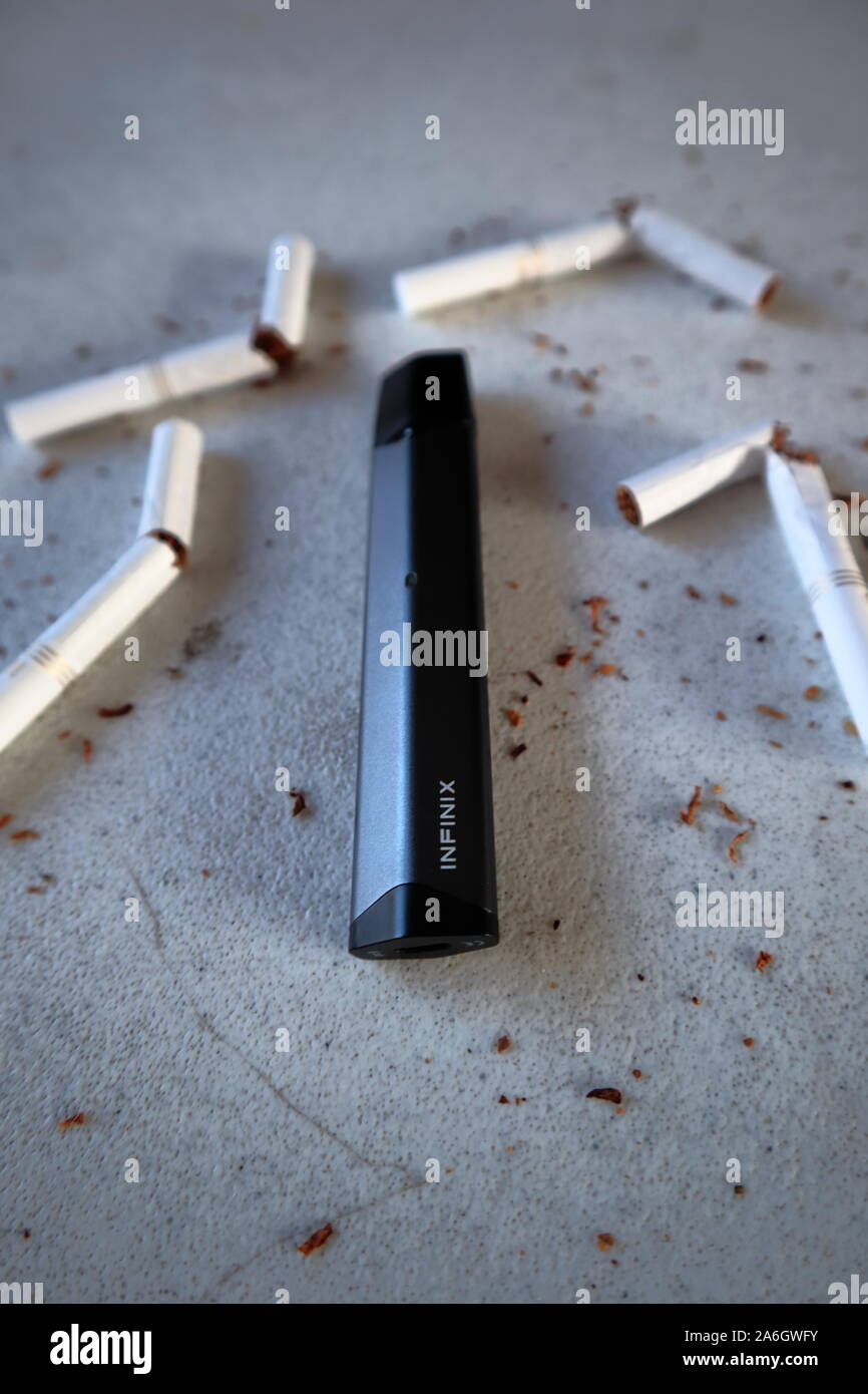 Vape device electronic cigarette smok infinix, as smoking alternative with broken marlboro gold cigarettes and scattered tobacco on white textured bac Stock Photo