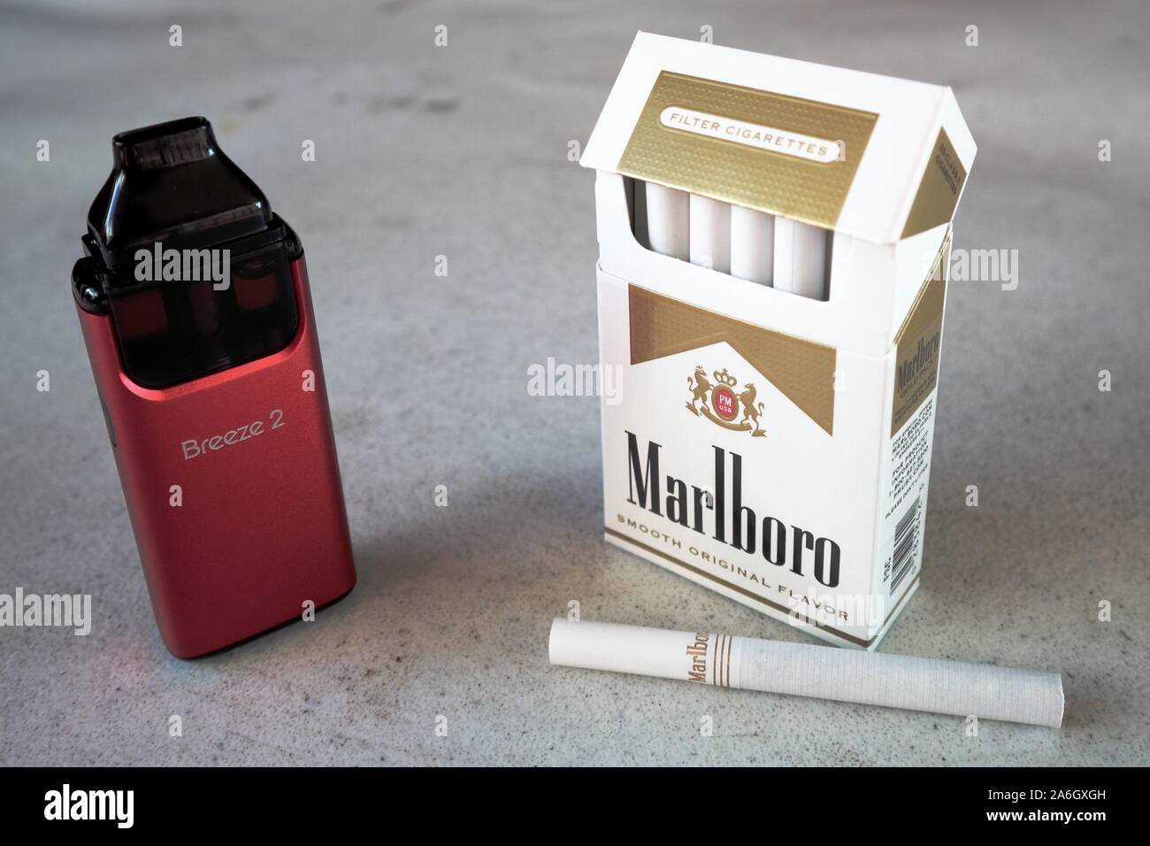 aspire breeze vape pod electronic cigarette device with a pack of marlboro cigarettes and one cigarette placed outside on a white textured table, isol Stock Photo