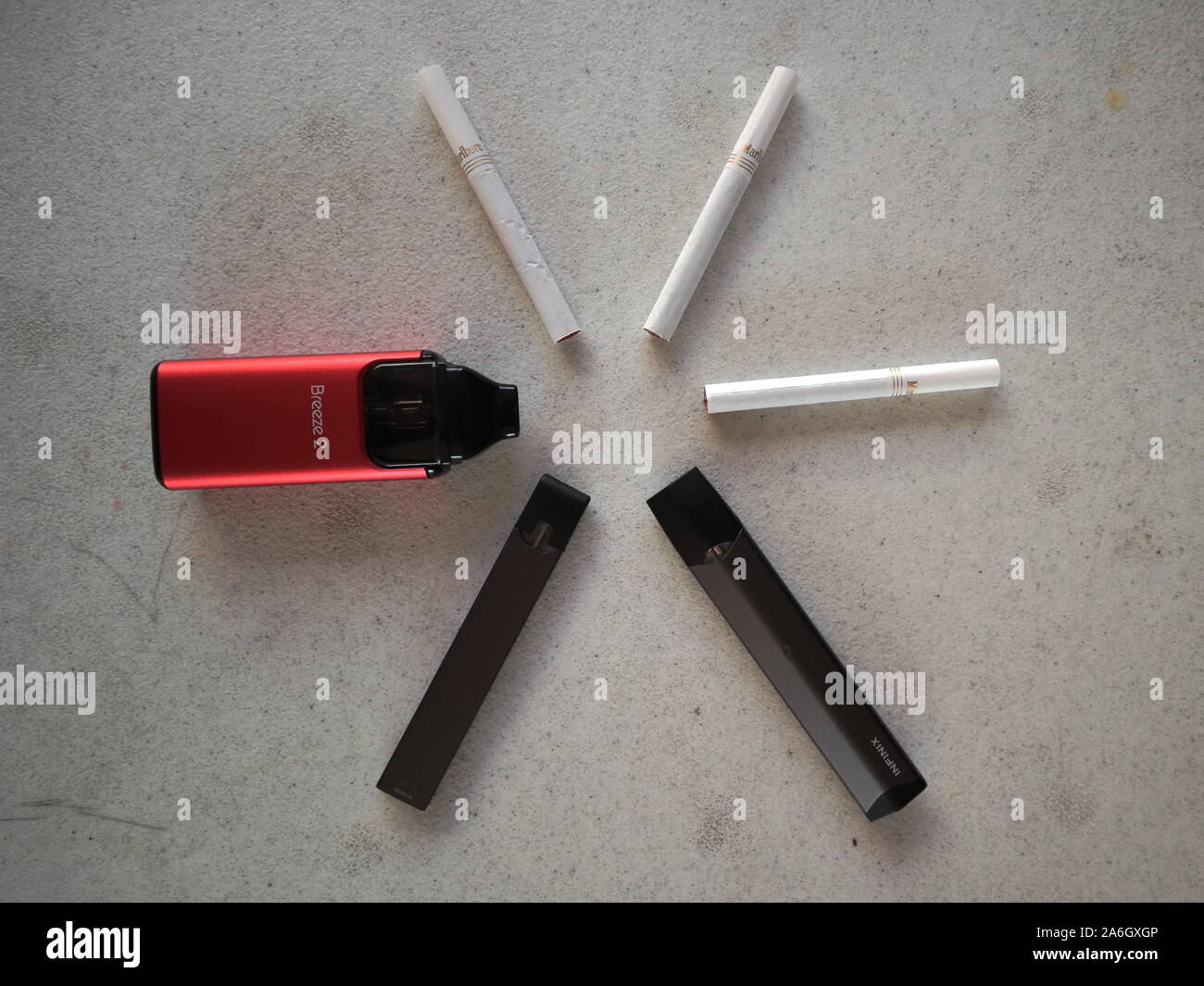3 vape electronic cigarette juul, aspire breeze, smok inifinix devices and 3 marlboro gold light cigarettes in a star pattern on a white textured back Stock Photo