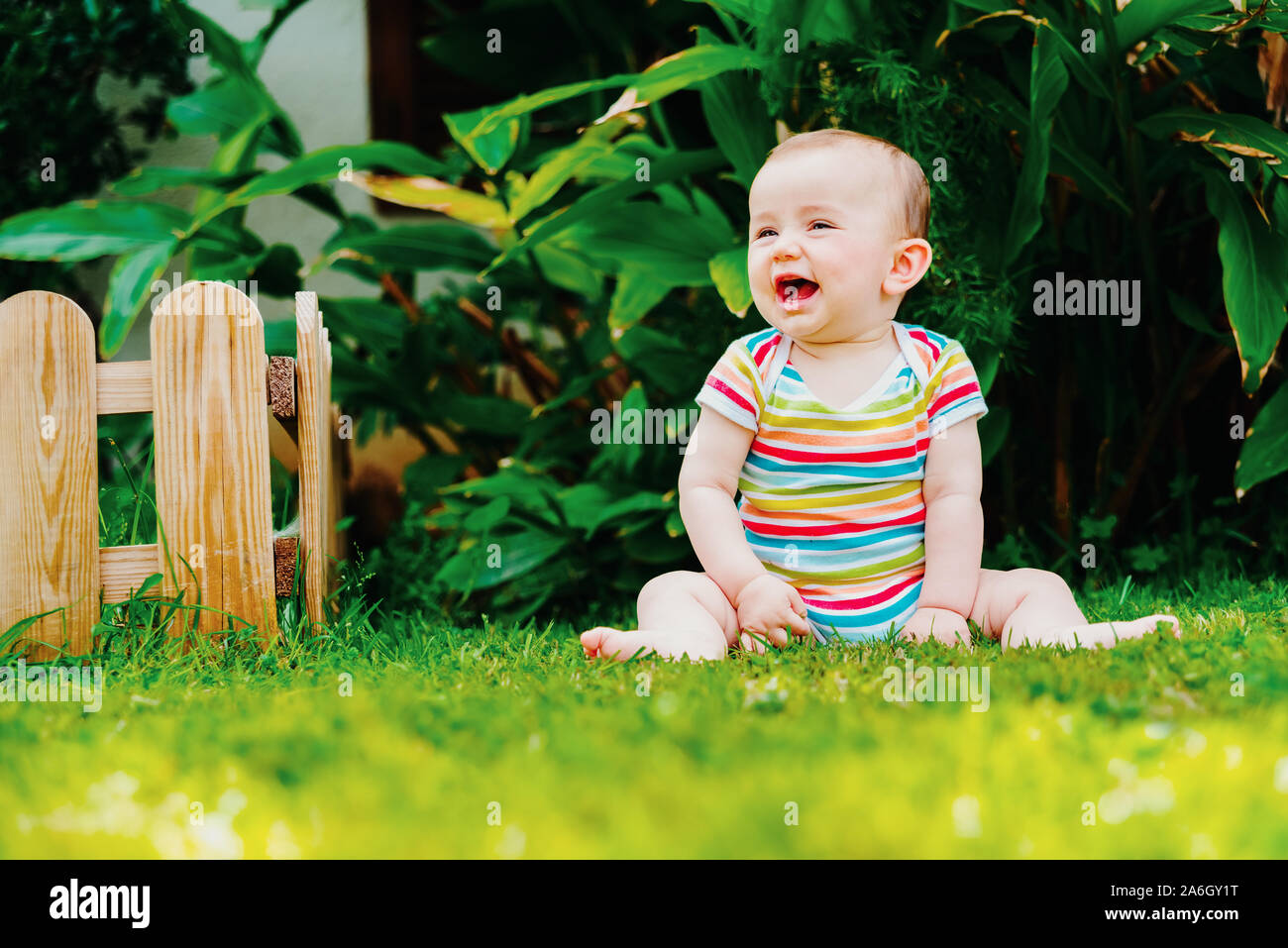 Lovely baby sitting on the grass laughing loudly Stock Photo - Alamy