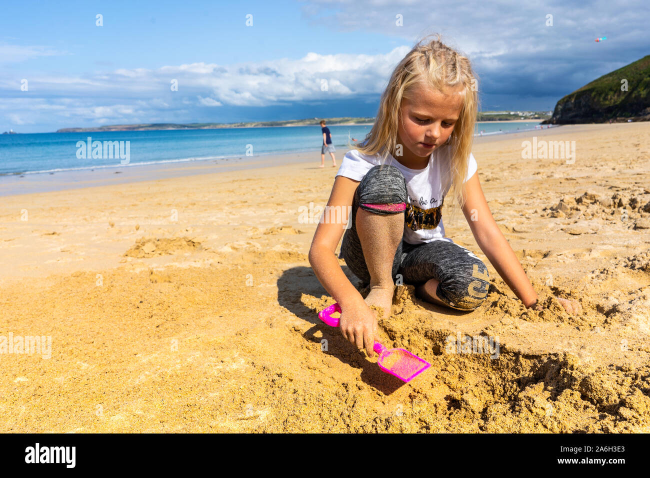 A pretty little blonde girl digging a hole on the beach with a spade at the beautiful Carbis Bay