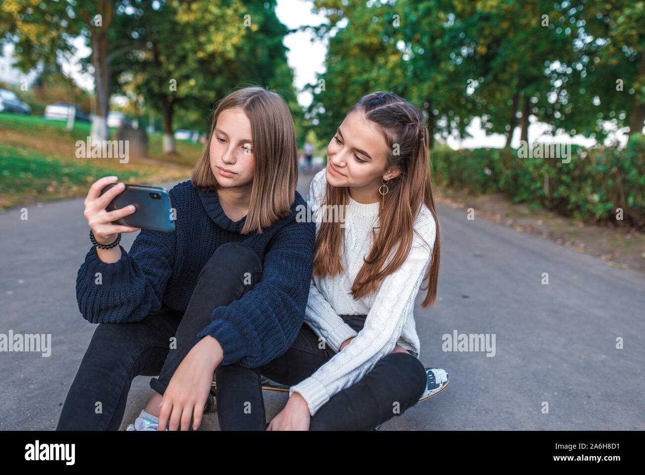 Two girls schoolgirls teenagers 12-15 years old, autumn day summer city  park, smartphone, selfie photo, video call, sweaters everyday clothes Stock  Photo - Alamy