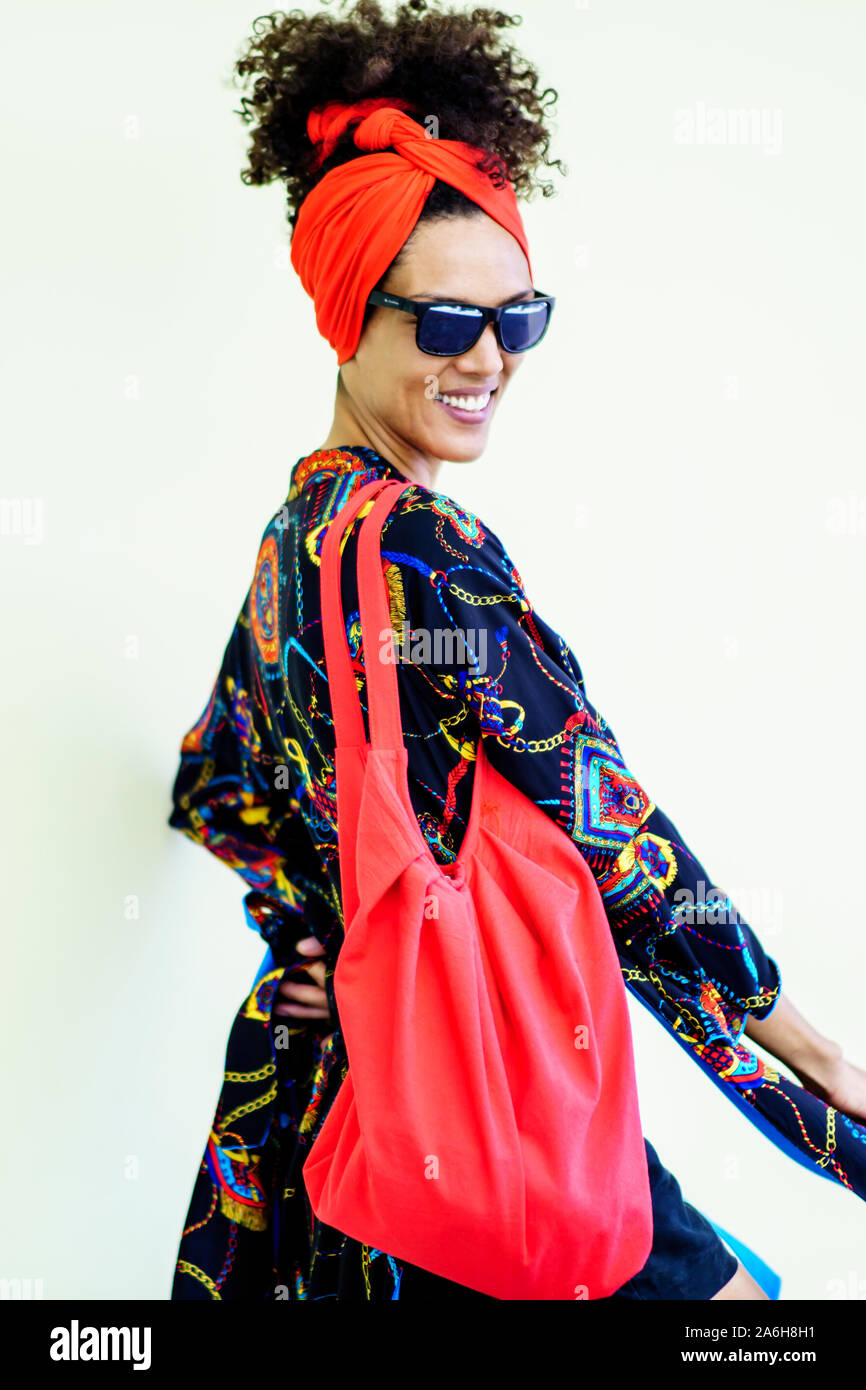 Cheerful woman with a afro hairstyle showing her beautiful red bag. Woman  wearing sunglasses and hippie clothes Stock Photo - Alamy