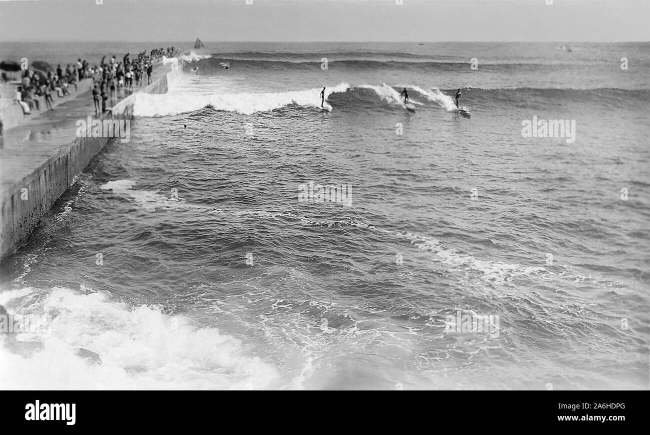 Surfers riding large waves c1930s/1940s along California's Corona del Mar jetty, adjacent to the world famous surf spot now known as the Wedge in Newport Beach. Stock Photo