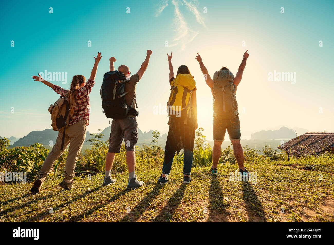 Four travelers or hikers stands with backpacks at sunrise against islands and sea Stock Photo