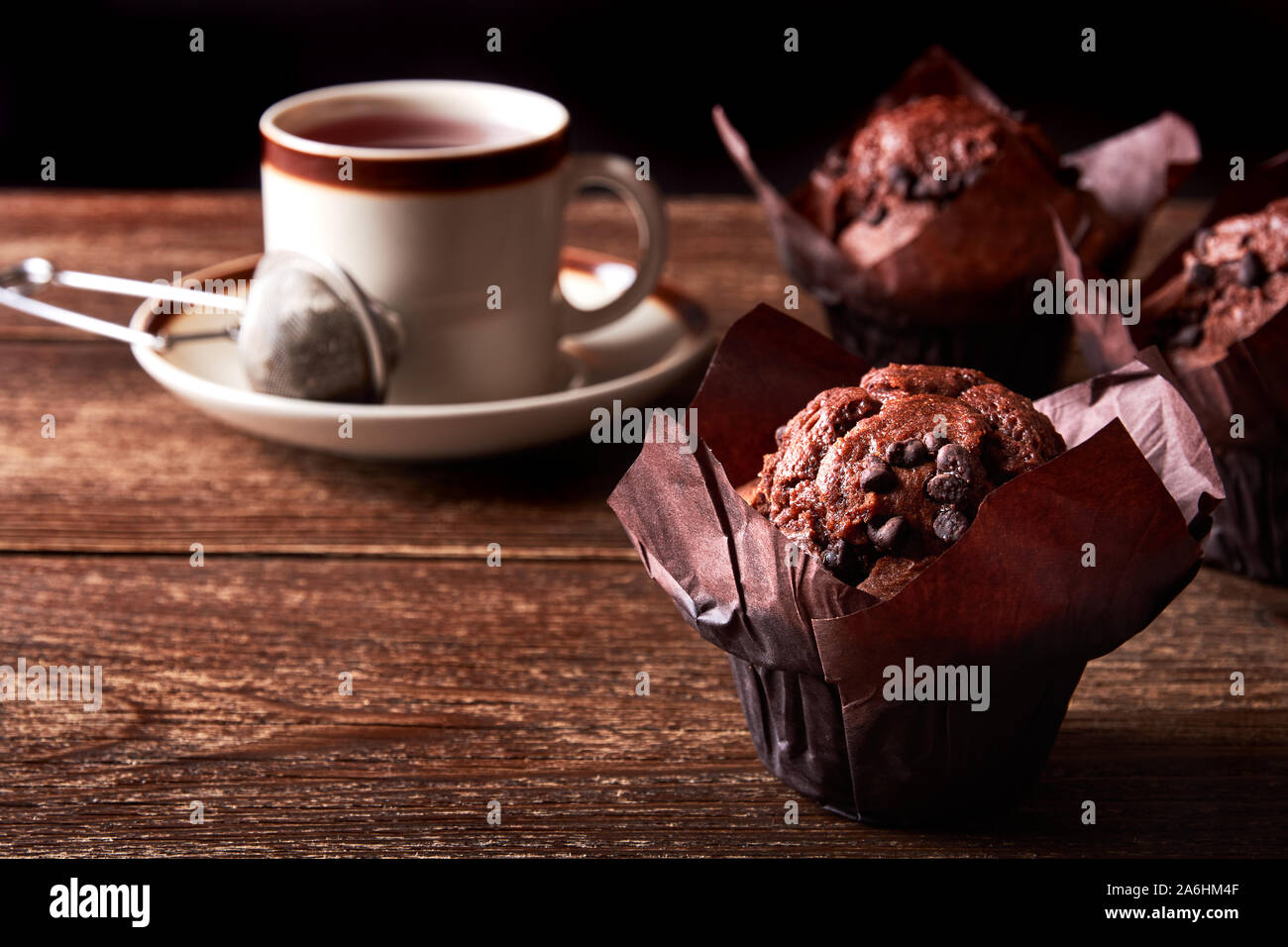 Still life with chocolate muffin and cup of tea on old wooden board table and with black background and space for text Stock Photo