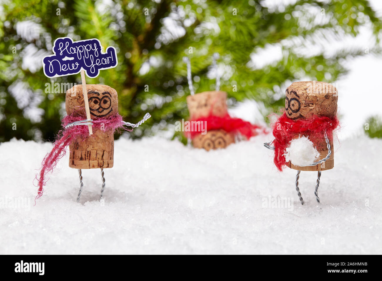 Funny champagne cork man on white snow wishes anybody 'happy new year'. His playful pal wants to play snowball fight, another is standing on the head. Stock Photo