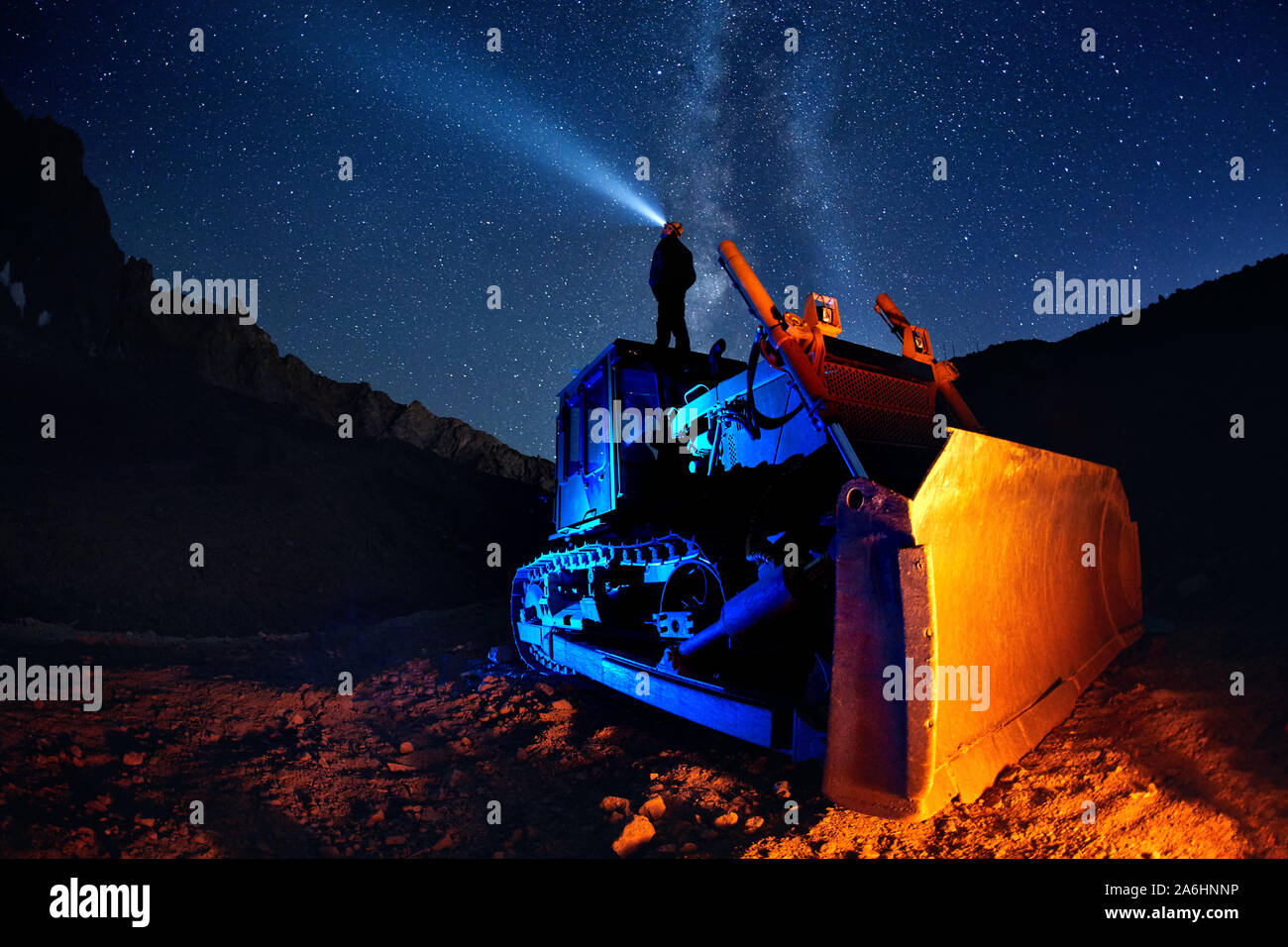 Man on bulldozer with head lamp under Milky Way view at night starry sky in the mountains Stock Photo