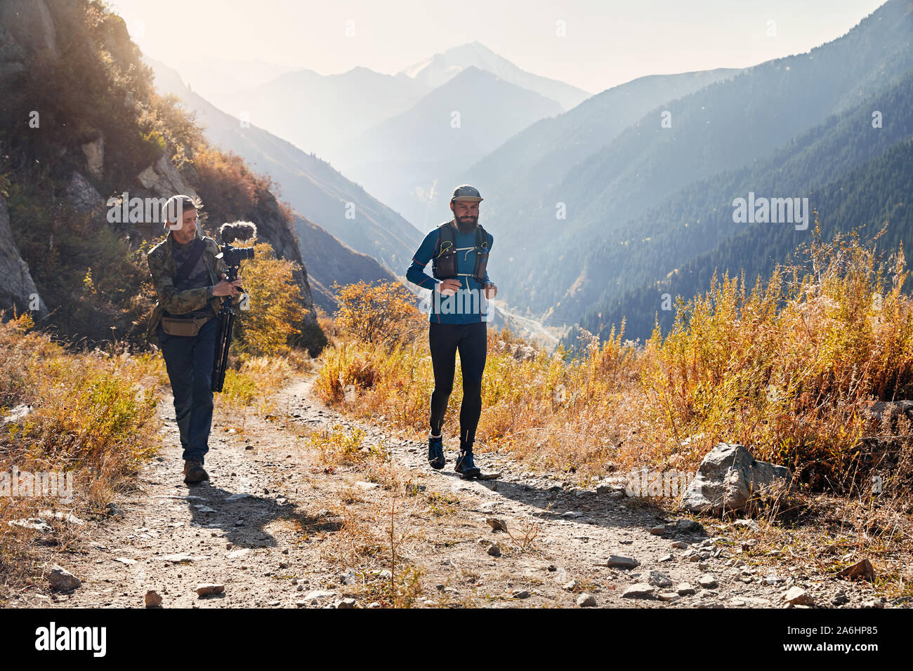 Filmmaker shooting documentary about runner athlete on the wild trail at mountains Stock Photo