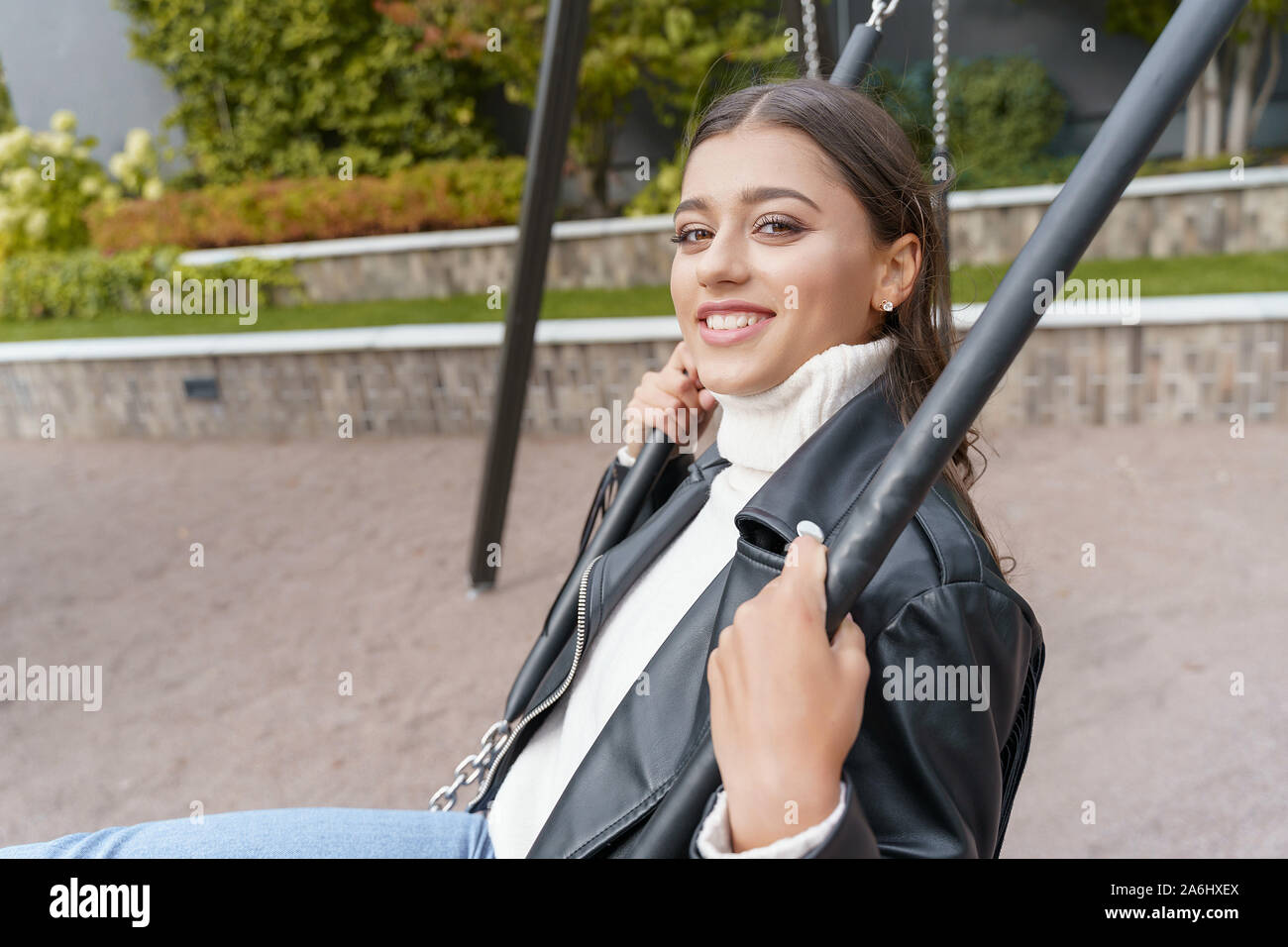 Beautiful young woman sitting on a swing and smiling Stock Photo - Alamy