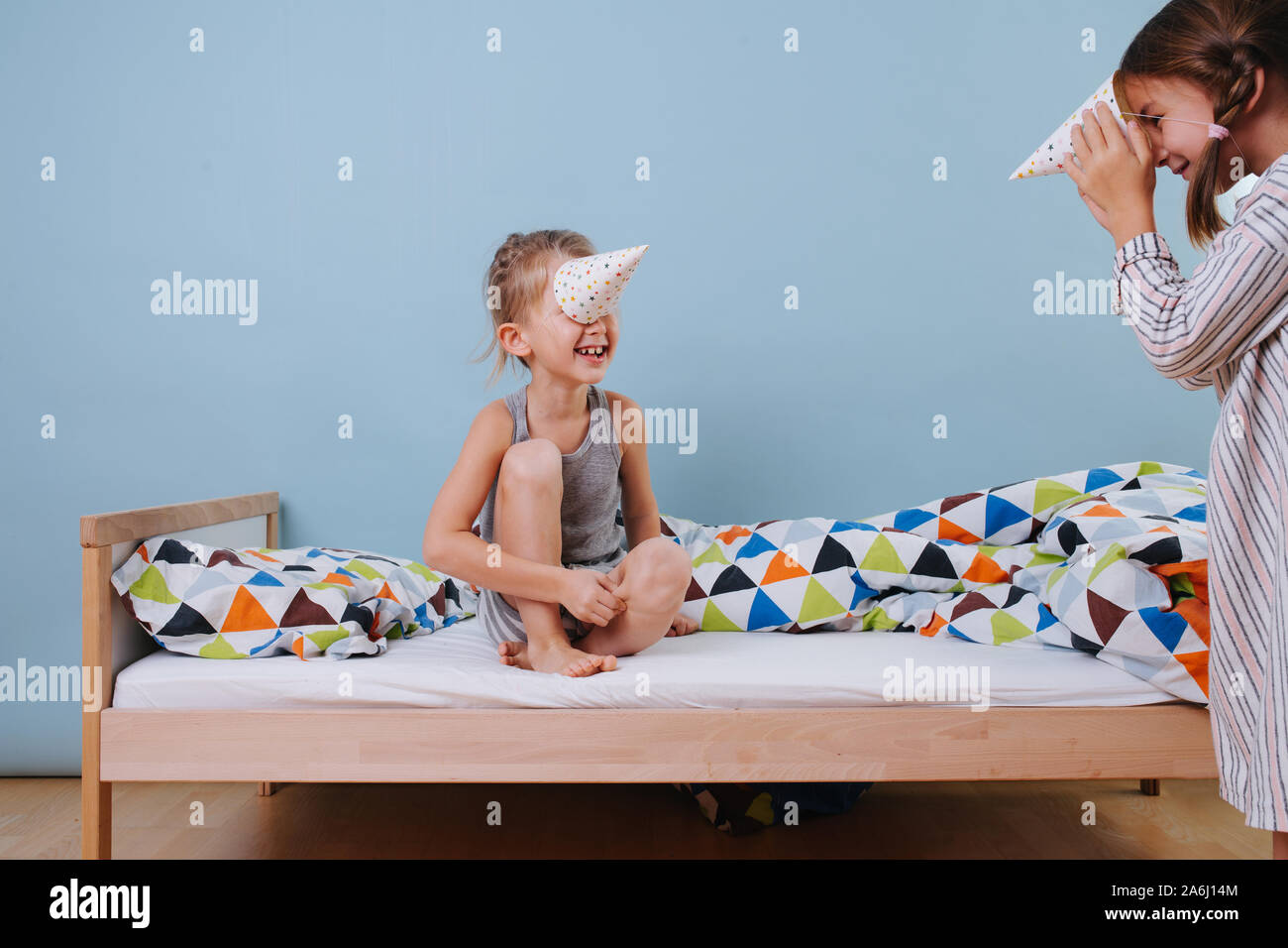 Boy and girl playing in bedroom with party cone hats, wearing them like horns Stock Photo