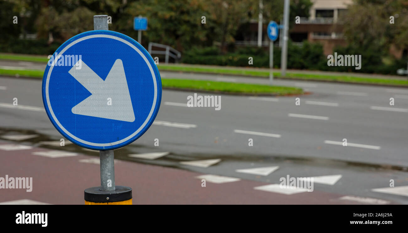 This way roadsign. Road sign one way, blue and round, white color arrow pointing direction right and down, lur street background, copy space Stock Photo