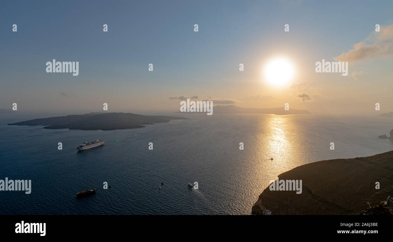 Fira, Greece - July 14 2019:   The sun setting over the islands of Santorini in the Aegean sea as seen from the cliff tops of Fira Stock Photo