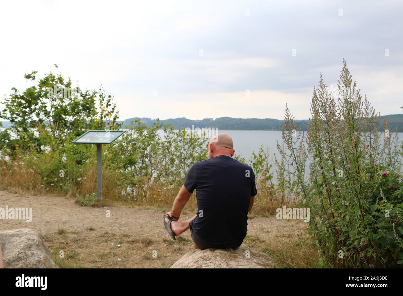 Man sitting on a stone on a high hill and looking on Vejle Fiord and Vejle Fiord Bridge is seen in Vejle , Denmark on 30 July 2019  © Michal Fludra / Alamy Live News Stock Photo