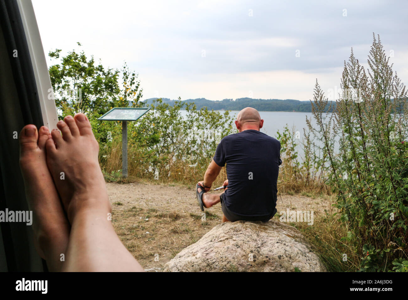 Man sitting on a stone on a high hill and looking on Vejle Fiord and Vejle Fiord Bridge is seen in Vejle , Denmark on 30 July 2019  © Michal Fludra / Alamy Live News Stock Photo