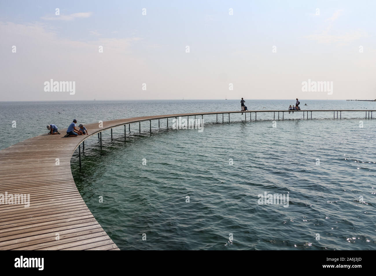 People walking by the The Infinite Bridge (Den Uendelige Bro) - circle shaped wooden pier built on a sea coast of a Aarhus Bay on a Varna Beach/Ballehage Beach, created by architect Niels Povlsgaard and Johan Gjødes  are seen in Aarhus, Denmark on 30 July 2019  © Michal Fludra / Alamy Live News Stock Photo