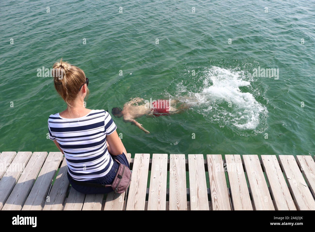 Man swimming around the Infinite Bridge (Den Uendelige Bro) - circle shaped wooden pier built on a sea coast of a Aarhus Bay on a Varna Beach/Ballehage Beach, created by architect Niels Povlsgaard and Johan Gj¿des are seen in Aarhus, Denmark on 30 July 2019 © Michal Fludra / Alamy Live News Stock Photo