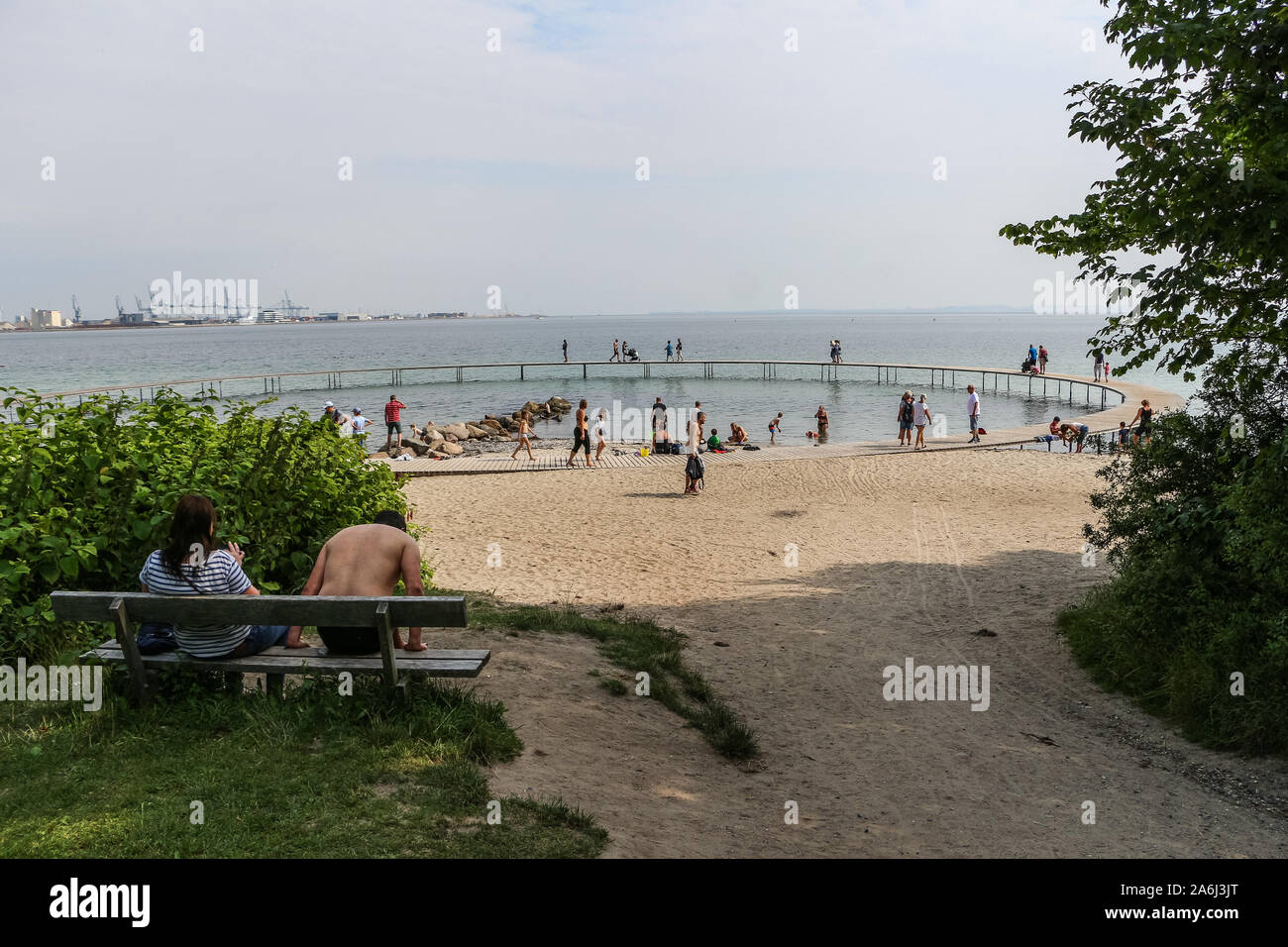 People walking by the The Infinite Bridge (Den Uendelige Bro) - circle shaped wooden pier built on a sea coast of a Aarhus Bay on a Varna Beach/Ballehage Beach, created by architect Niels Povlsgaard and Johan Gjødes are seen in Aarhus, Denmark on 30 July 2019 © Michal Fludra / Alamy Live News Stock Photo