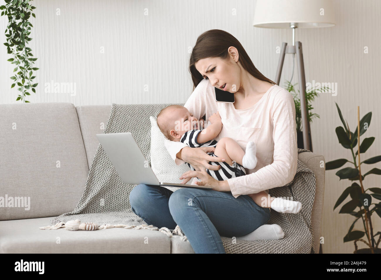 Mother holding crying baby and calling to pediatrician for advice Stock Photo