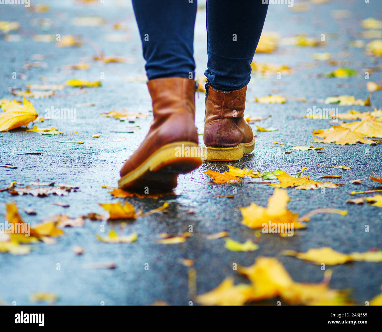 Walk on wet sidewalk. Back view on the feet of a woman walking along