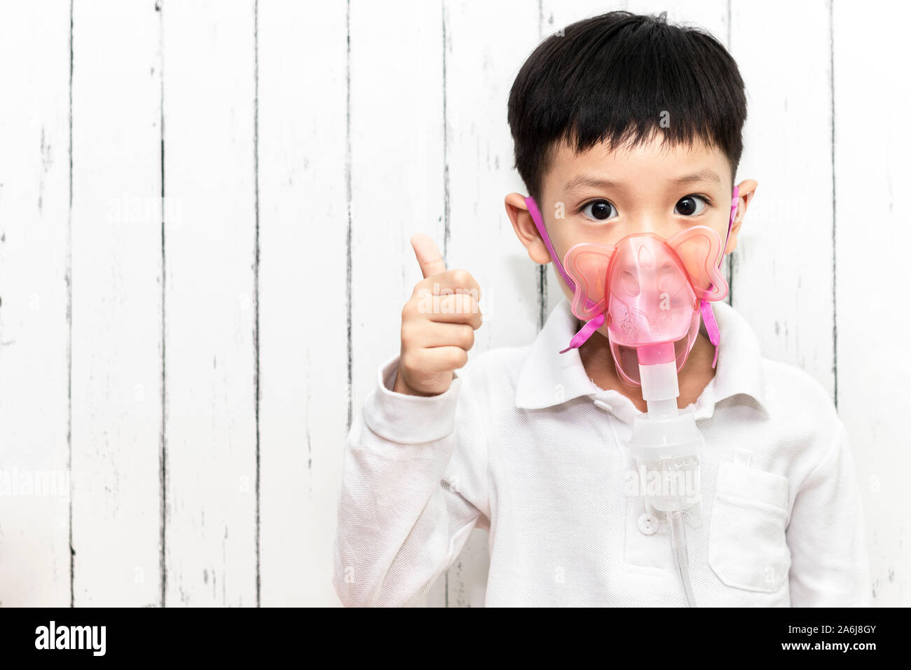 Asia boy using nebulizer and inhaler for the treatment. Little child making inhalation with nebulizer at hospital. Little boy show a thumbs up. Stock Photo