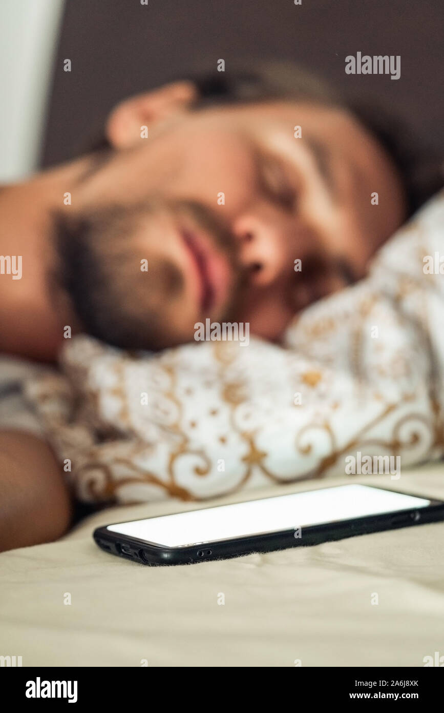 Closeup photo of a young man sleeping in bed. Mobile phone with a