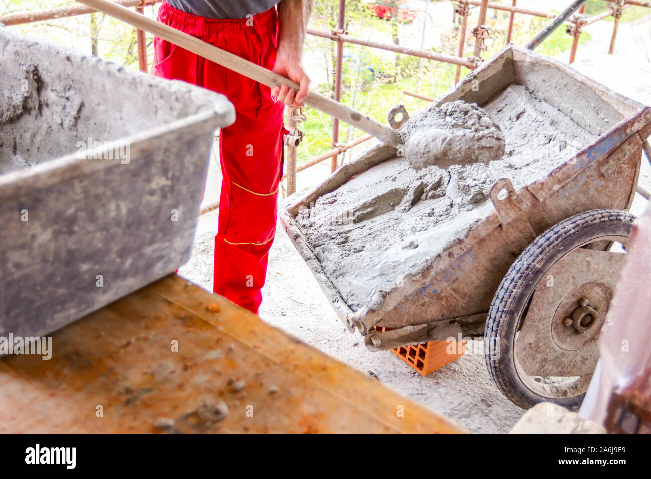 Construction worker is using shovel to unloading cement, mortar, from wheelbarrow on construction site. Stock Photo