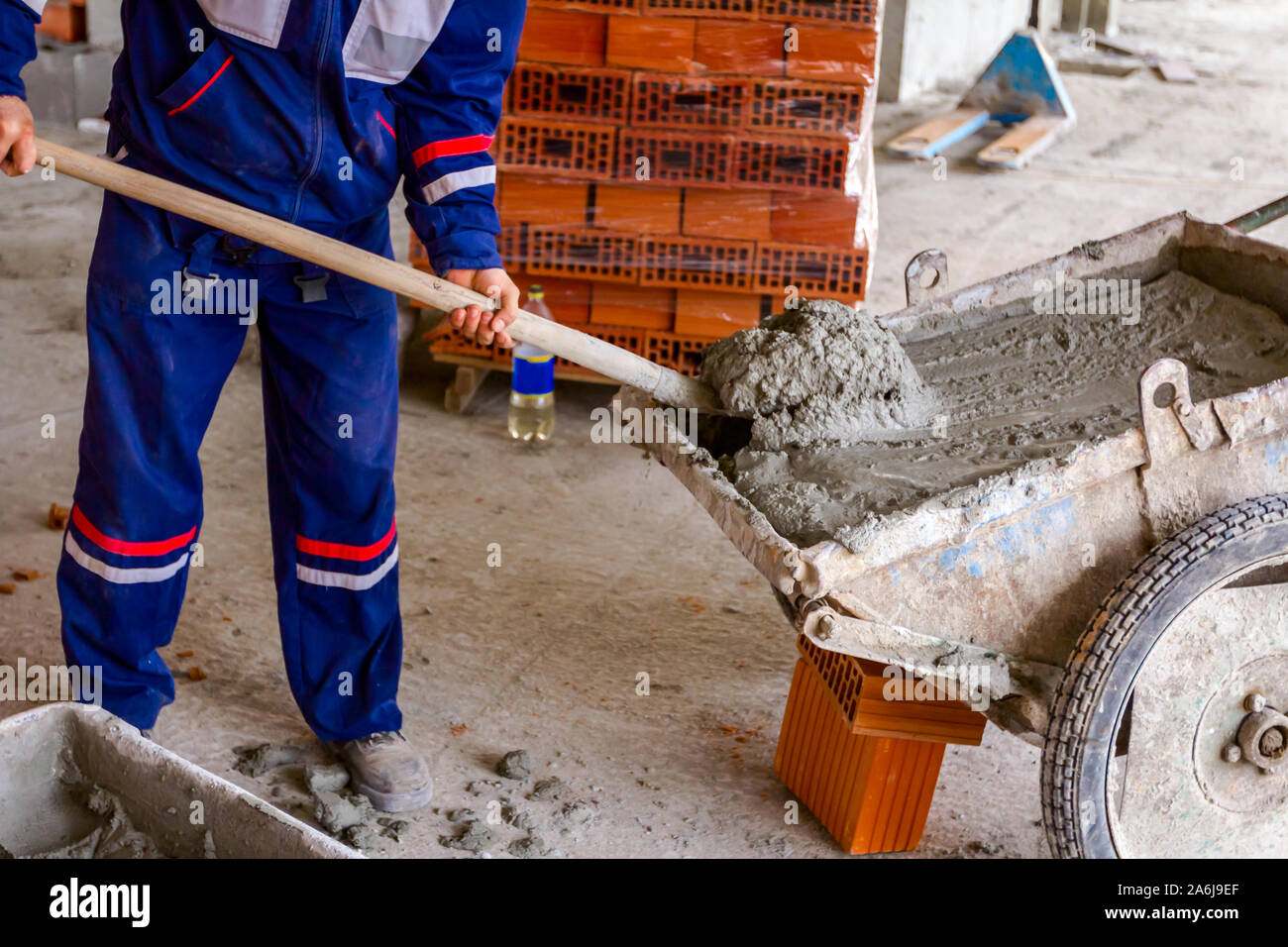 Construction worker is using shovel to unloading cement, mortar, from wheelbarrow on construction site. Stock Photo