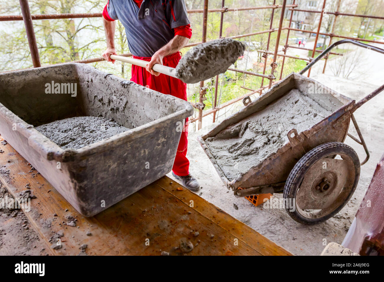 Construction worker is using shovel to unloading cement, mortar, from wheelbarrow on construction site. Stock Photo