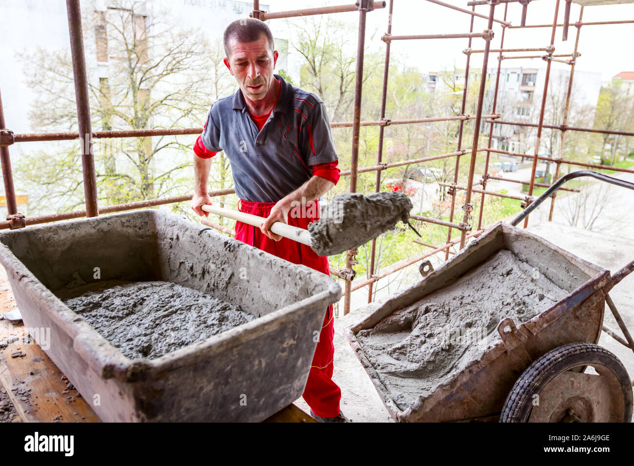Construction worker is using shovel to unloading cement, mortar, from wheelbarrow on construction site. Stock Photo