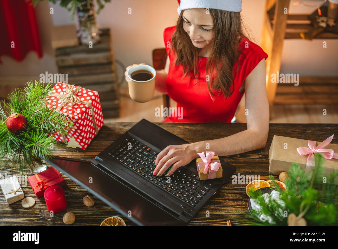 Beautiful woman in a red dress receives a gift via the Internet for the New year. Online shopping for Christmas holidays. Stock Photo