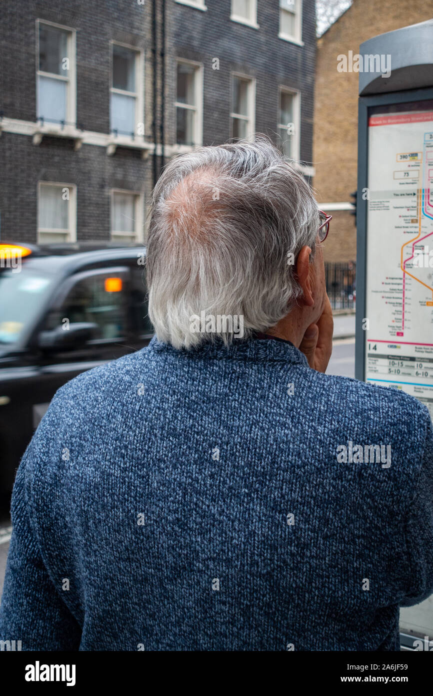 middle-aged man looking at bus time table at bus stop Stock Photo
