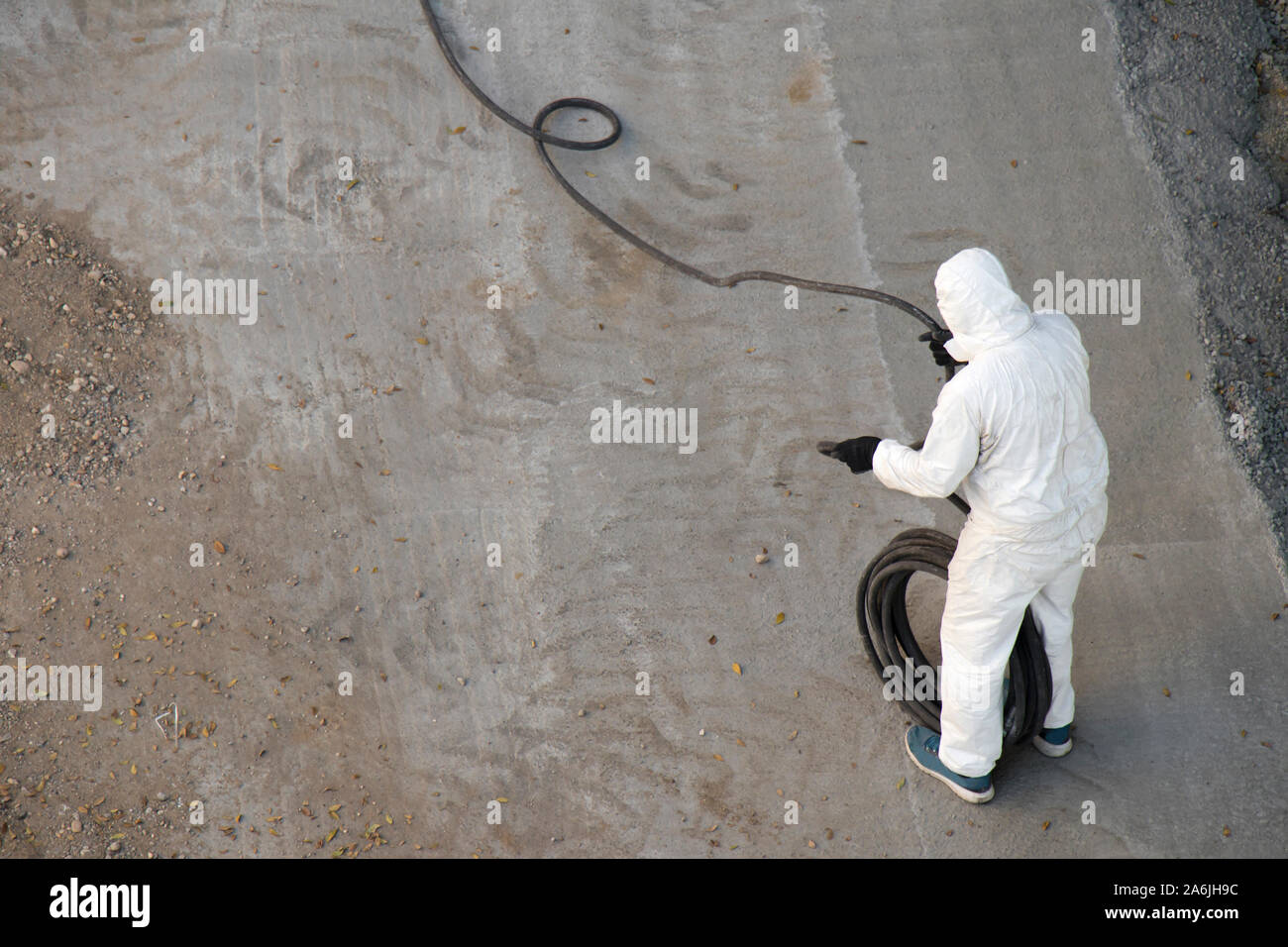 Construction worker in white protective  jumpsuit wrapping a long hose, from above Stock Photo