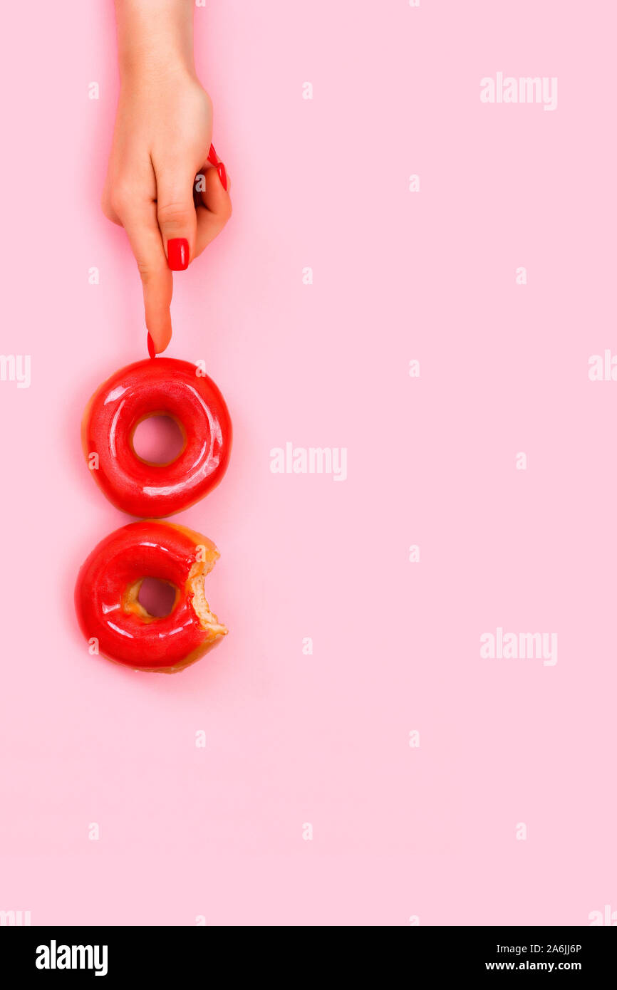 A female hand with a beautiful stylish manicure holds two donuts with sparkles on a finger. Pink background, top view. Stock Photo