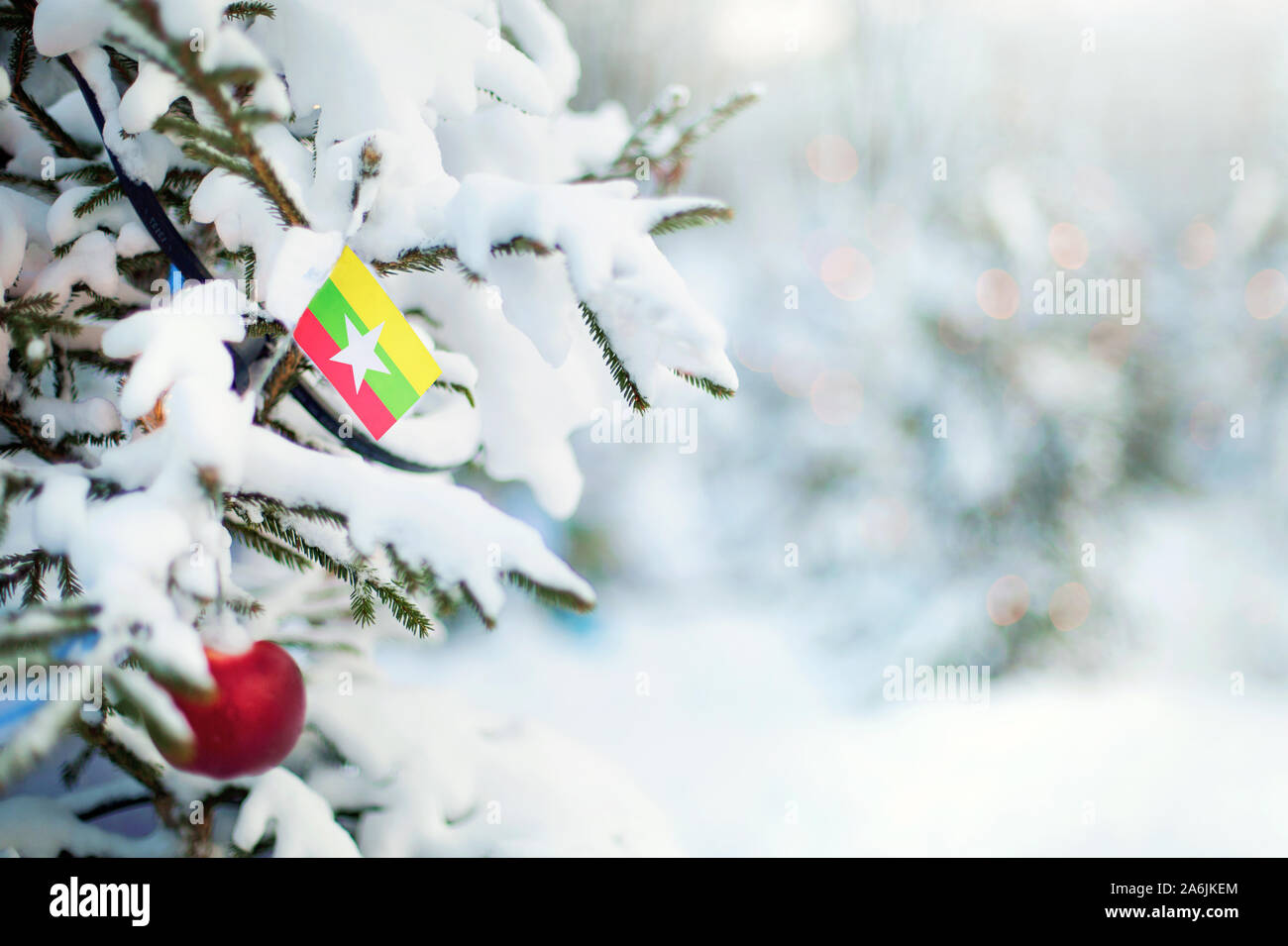 Christmas Myanmar. Xmas tree covered with snow, decorations and a flag