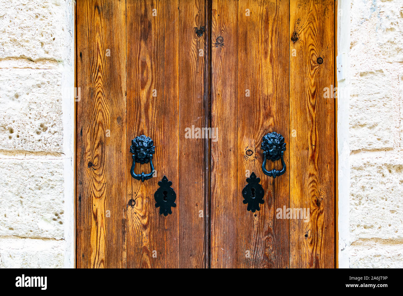 Natural wooden door with black vintage knockers as lion heads and black ornately shaped key-holes. Wooden door with black hardware. Stock Photo