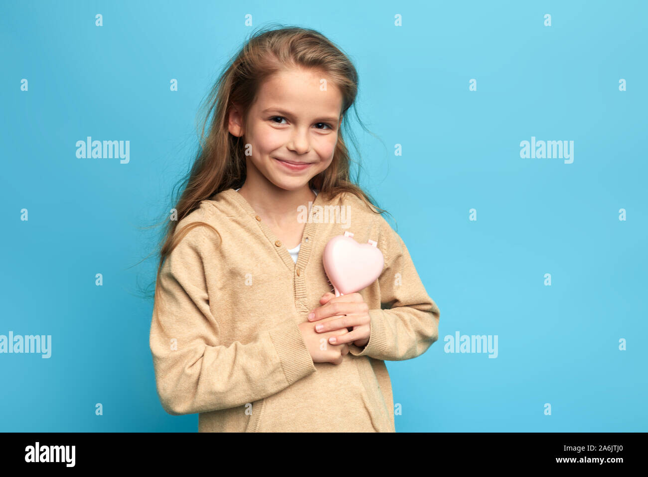 little smiling girl in sweater brushing her hair, preparing for a party, holiday. close up portrait, isolated blue background, studio shot, lifestyle, Stock Photo