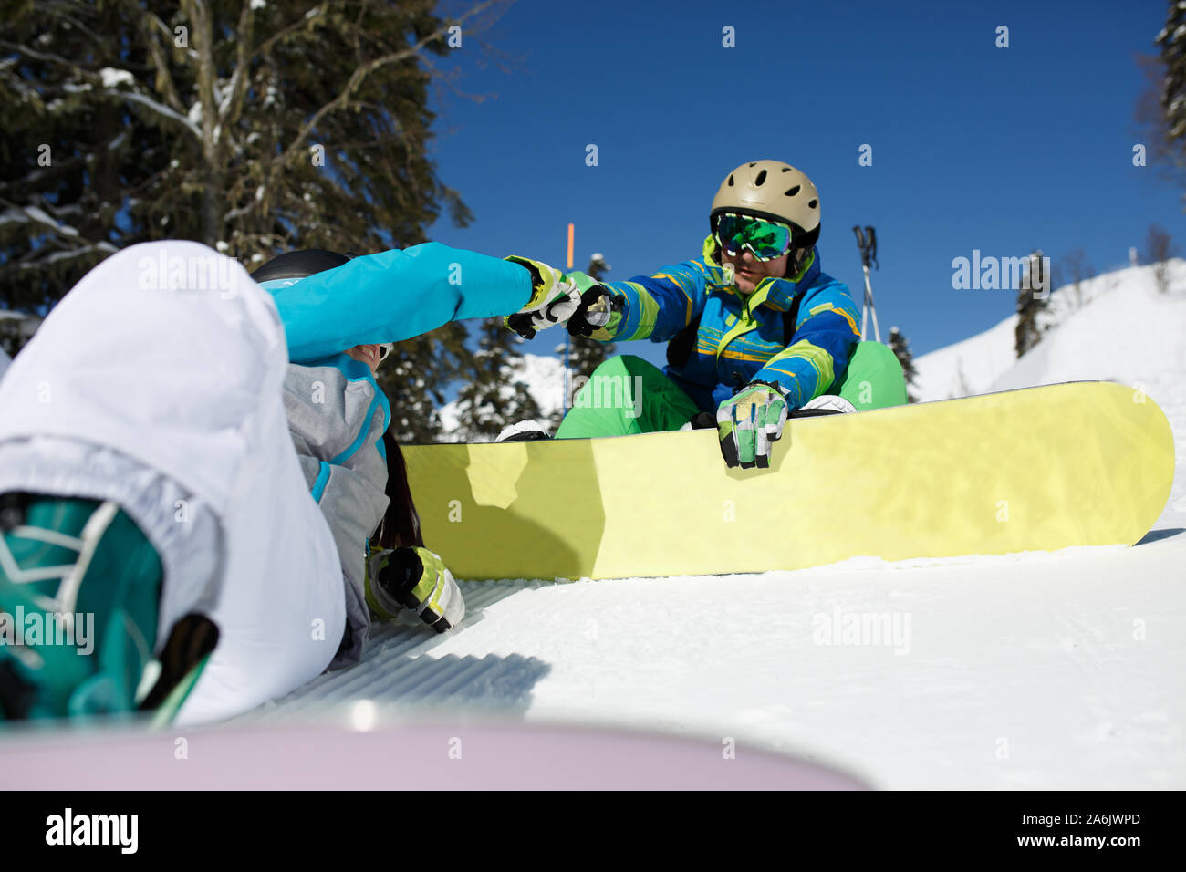 Masked woman sitting on hillside doing handshake with man with snowboard on winter day Stock Photo