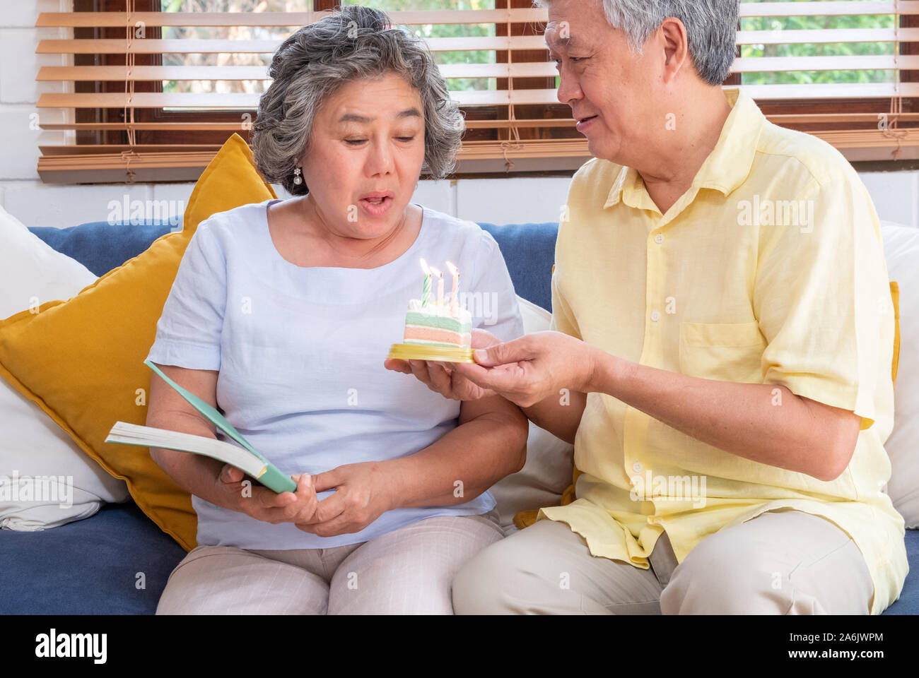 asian senior man surprise senior woman with birthday cake in living room at home.aging at home concept. Stock Photo